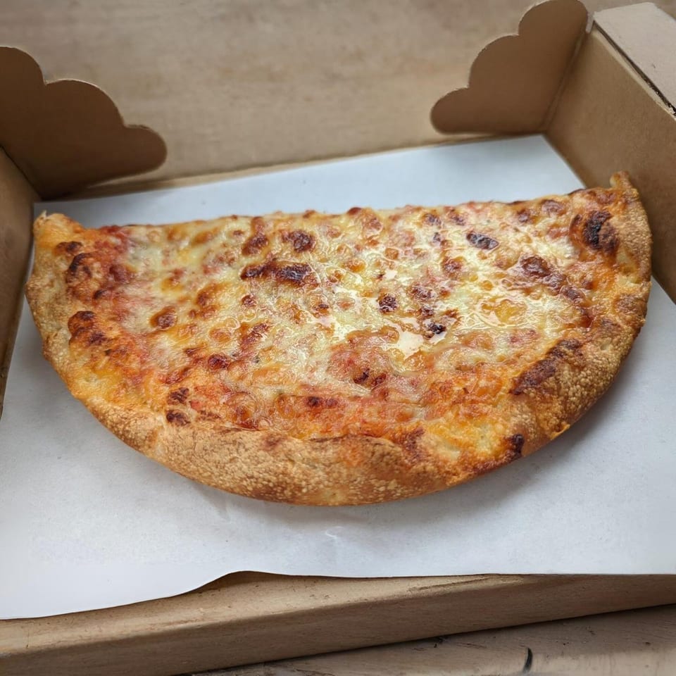 A half-moon shaped cheese pizza, golden brown and bubbly, rests inside a cardboard takeout box.