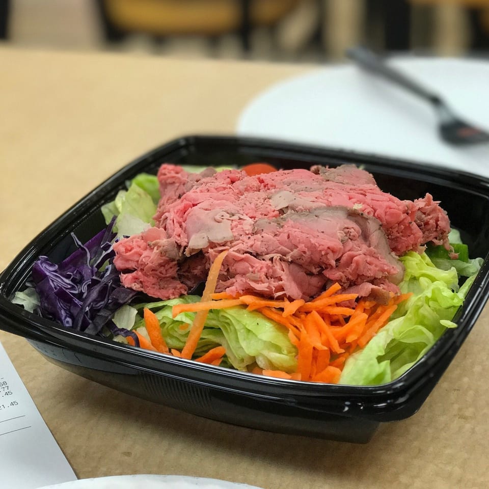 Roast beef salad with lettuce, shredded carrots, and purple cabbage in a black container.