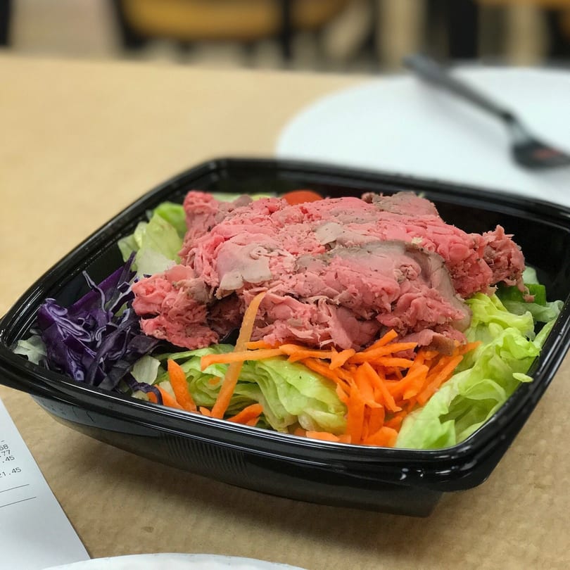 Roast beef salad with lettuce, shredded carrots, and purple cabbage in a black container.